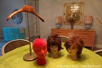 Three vintage store display items shown on a table: two vinyl mannequin heads with wigs and one bright fuchsia pink crushed velvet head on a wooden extender with metal base