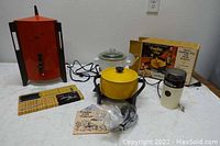Lot of 4 kitchen appliances including fondue pot in box, yellow small crock pot, orange coffee pot, and Regal coffee grinder