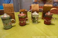 All four Japanese tea cups with lids and inserts displayed on table with their original boxes behind them.