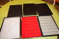 Six jewelry display trays arranged on a flat surface, showing felt linings in white, red, light gray, and dark colors and separated glass covers.