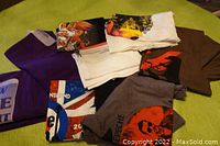 Overview of eight folded and stacked assorted band concert T-shirts on green surface