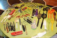 Table spread with a large quantity of diverse kitchen utensils and serving flatware, showing full lot contents