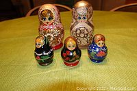 Five wooden nesting dolls with white and gold paint, detailed hand-painted faces and floral designs, arranged on green fabric surface.