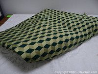 Folded mid-century modern upholstery fabric with geometric 3D green box pattern displayed on table showing textured weave and pattern detail.