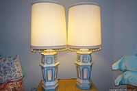 Photo showing the pair of tall plaster lamps illuminated with their shades on, highlighting the height and general design.