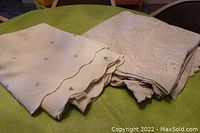 Pair of two vintage matelassé coverlet blankets folded on green surface showing off-white/tan grey paisley pattern and white coverlet with green clover shamrocks.