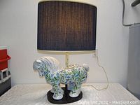 Front view of the ceramic horse lamp with the navy blue pleated shade on table against wall.