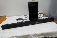 Photo showing the Samsung soundbar speaker on a tabletop with wired connections and wireless active subwoofer behind it, highlighting overall condition and setup.