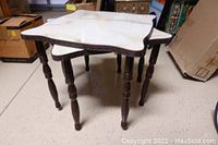 Two vintage nesting tables stacked, showing white faux marble tops, decorative edges and scrolly dark wooden legs.