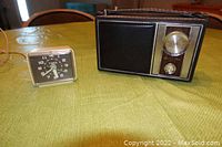 Both the TOPP Juliette portable radio and TIMEX alarm clock shown on a table, radio black with gold knobs and clock square with black face.