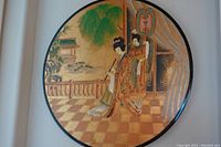 Full image of the round hanging wall plaque with black lacquer rim depicting two Asian women in traditional dress and garden background