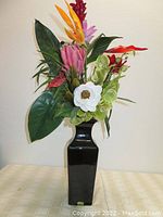 Black pottery vase with tall silk flower bouquet displayed showing front view of arrangement and vase shape.
