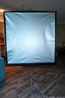 Front view of the vintage movie projection screen set on a tripod stand with screen fully extended.