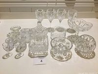 Full collection of assorted cut glass and crystal glassware laid out, showing multiple stemmed glasses, bowls, dishes, basket, and decanter.