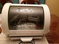 Front view of white Baby George rotisserie oven with transparent door and George Foreman signature logo.