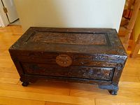 Full view of the large dark wood carved storage box on wooden floor, showing rectangular shape and claw feet.