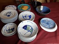Overview photo showing multiple ceramic dishes and bowls on a red cloth, including fish motif dishes and colorful plates.