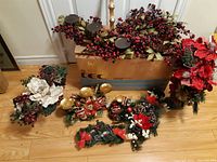 Overview of multiple Christmas arrangements, candle holders, berry greenery, and box with assorted decorations on floor