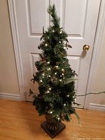 Full view of the small artificial Christmas tree with lights and decorations placed indoors on a hardwood floor.