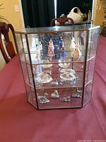 Front view of the glass and metal display cabinet showing porcelain figurines and glass swan figurines inside.