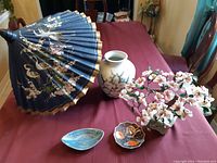 Photo showing blue paper umbrella, ceramic vase with floral design, jade bonsai tree, and two small plates on table.