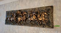 Full view of the large rectangular bronze-colored 3D wall art depicting Roman warriors on horses in motion, mounted on a wall.