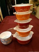 Stacked 5 Pyrex orange nesting bowls with white wheat pattern and 2 smaller white bowls with blue snowflake pattern next to stack.