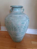 Front view of the large terra cotta vase showing spiral and leaf carved designs and two handles at the neck.