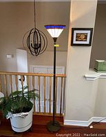 Full view of floor lamp showing dark metal base and stand with a cone-shaped stained glass shade with brown, blue, and white glass panels.