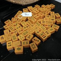 Partial set of 82 amber colored Bakelite Mahjong tiles arranged on a dark surface, showing various traditional Mahjong symbols in colored inlay.