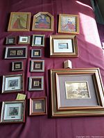 Overview photo of 17 framed miniature paintings and prints arranged on a red fabric surface showing various sizes and styles, including three main paintings with gold leaf.