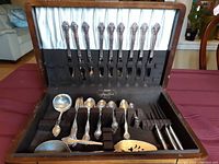 Photo of fitted case with silverplated forks, knives, spoons, teaspoons and serving utensils in black fitted slots with satin lined case lid