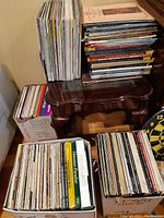 Photo showing four large stacks of vinyl LPs and boxed sets on floor and table, mostly classical titles visible.