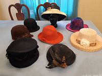 Seven women's hats displayed on a table showing variety of colors, materials, and decorations