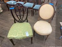 Two antique chairs, one with green patterned upholstery and ornate backrest, one with beige circular padded seat and backrest.