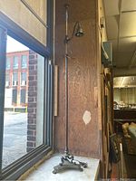 Full side view of the tall antique floor lamp placed near a window showing its height and curved light arm.