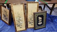 Photo showing three framed items: two tall vertical traditional Asian floral paintings with ornate gold-tone frames; and one smaller framed shadow box with white carved floral designs on a black background.