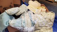Overview of box with multiple blankets and linens in different colors, including yellow, blue, and patterned comforters in plastic bags.