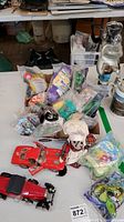 Overview of the lot on a table showing multiple Happy Meal toys in sealed bags, two red die-cast model cars, and a chef plush toy.