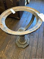View of the cast iron bowl stand showing the circular top ring with vintage wear and rust patina, placed on wooden floor near antique chests.