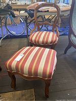 Front view showing vintage balloon back wooden chair with red and cream striped upholstery and matching ottoman with casters.