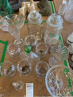 Top-down view showing two tall lidded jars, multiple small glass jars and vases, and a crystal dinner bell on a table.
