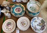 View of a variety of plates and two ornate vases showing floral patterns and border colors.