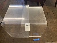 Two clear Lucite nesting tables stacked together on a wooden floor, showing the curved design and glossy finish.