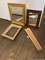 Three mirrors or frames and four wooden tapered table legs, displayed on wooden floor