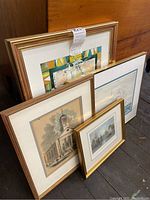 Four framed prints leaning against wooden wall, varying sizes and frame styles