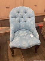 Front view of occasional chair showing tufted upholstery, wooden legs with casters, and overall chair shape and color.