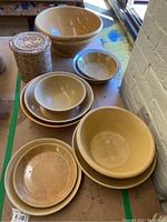Eleven pottery pieces including large and medium bowls, plates, and brown spongeware crock arranged on a table.
