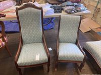 Two vintage wooden chairs, a rocking chair and a side chair, upholstered in light blue fabric with white cross patterns. Both have carved wooden frames and legs.