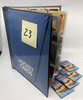 Blue hockey card album standing slightly open with 4 sealed wax packs stacked next to it.